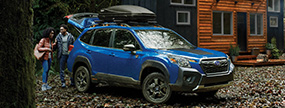 Couple unpacks their Subaru after arriving at their log cabin in the woods