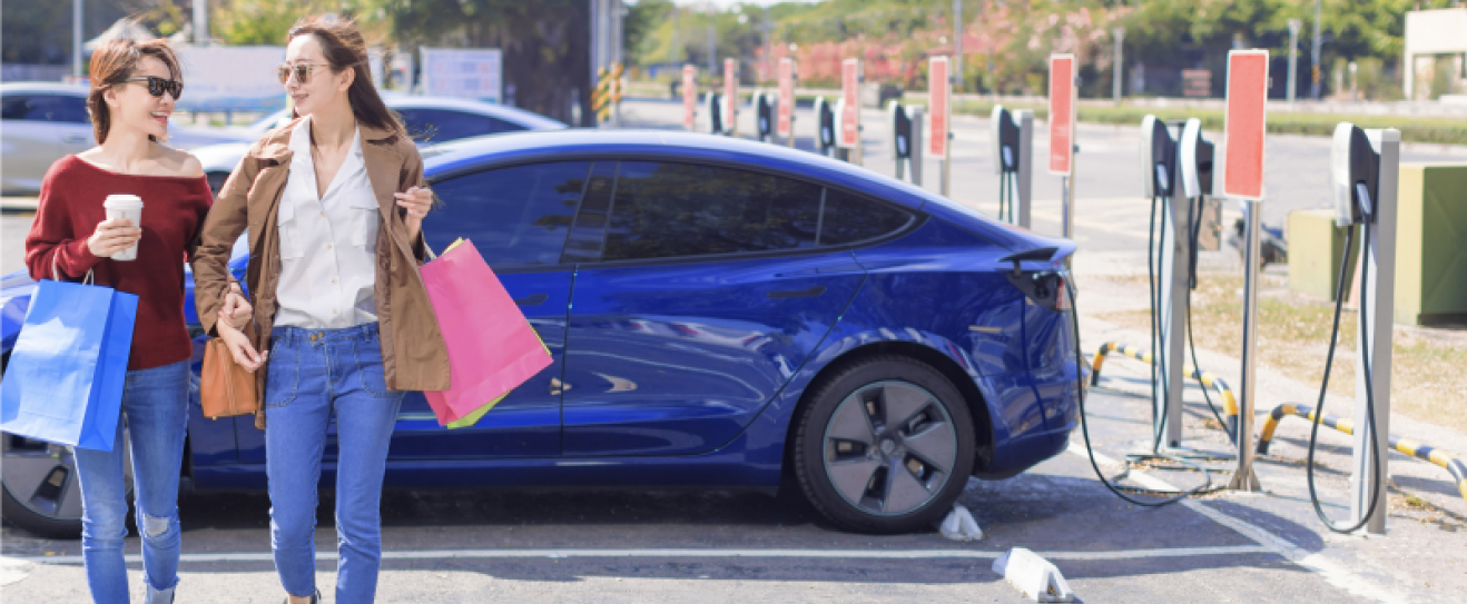 Two women walk away from their Subaru electric vehicle as it charges in a parking lot