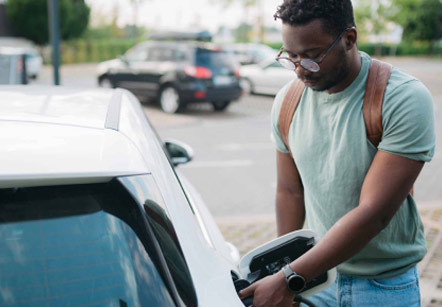 A man stands by his car plugging in the charger for his electric vehicle