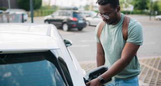 A man stands by his car plugging in the charger for his electric vehicle