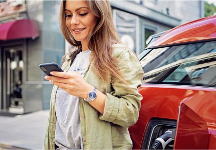 A woman looks at her phone next to her Subaru electric vehicle as it charges