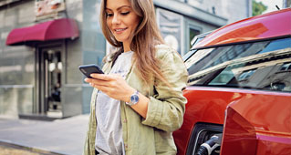 A woman looks at her phone next to her Subaru electric vehicle as it charges