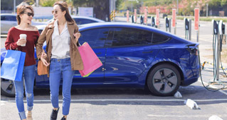 Two women walk away from their Subaru electric vehicle as it charges in a parking lot