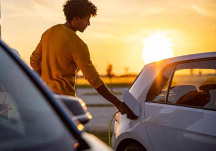 A man attaching the charger from an electric vehicle charging port in front of a sunset