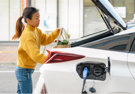 A woman loads groceries into the trunk of a Subaru electric vehicle as it charges