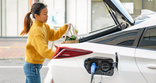 A woman loads groceries into the trunk of a Subaru electric vehicle as it charges