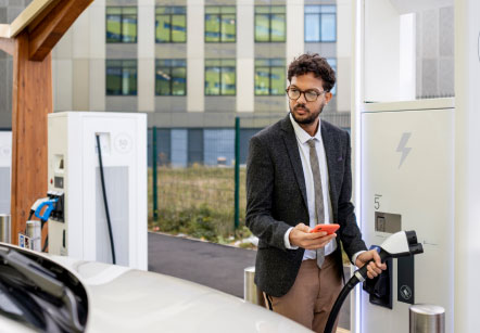 A man detaching the charger from an electric vehicle charging port and bringing it towards his car