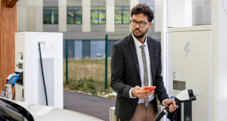 A man detaching the charger from an electric vehicle charging port and bringing it towards his car