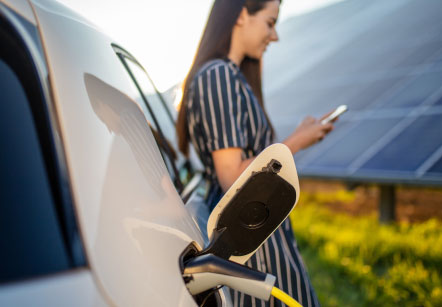 A woman leans against her Subaru electric vehicle as it charges