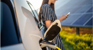 A woman leans against her Subaru electric vehicle as it charges