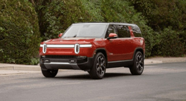A Rivian R1S driving in front of greenery 