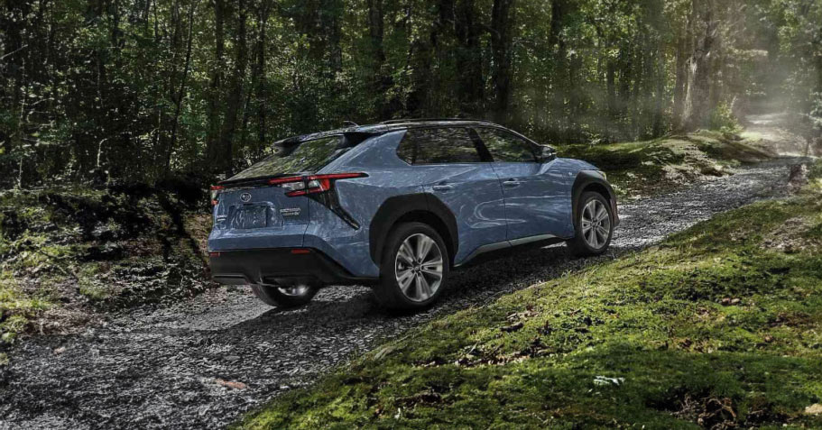 A Subaru electric vehicle drives up a dirt road through a forest