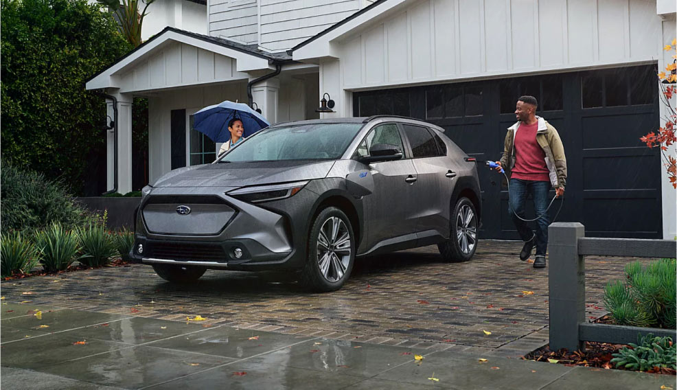 A man walking towards his electric vehicle parked in front of his home, charger in hand